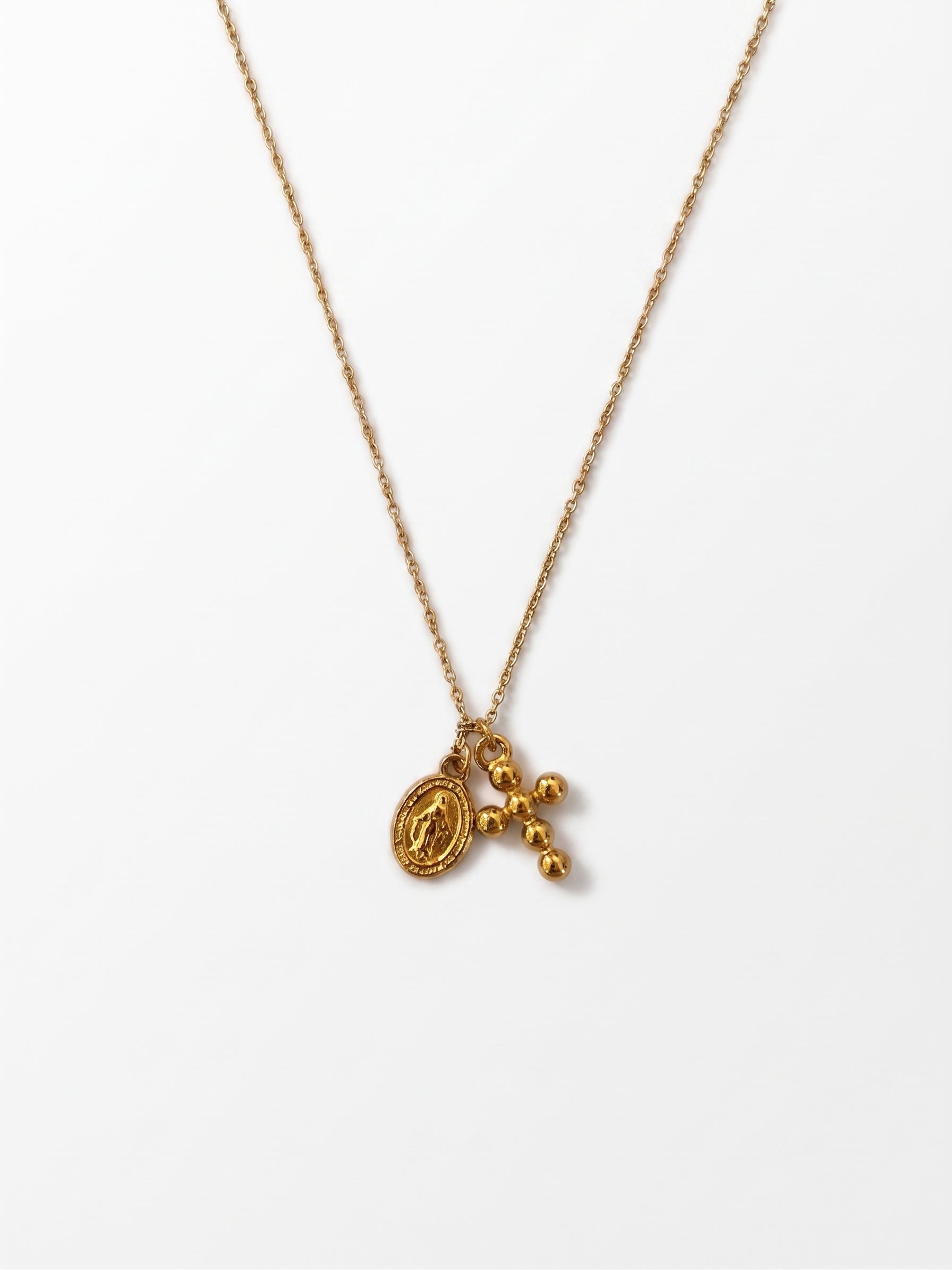 A delicate gold chain necklace featuring a small oval medallion and a dangling cross with three small beads, displayed against a clean white background.