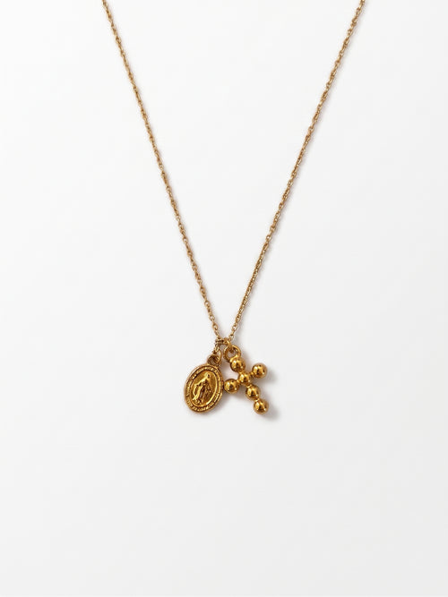 A delicate gold chain necklace featuring a small oval medallion and a dangling cross with three small beads, displayed against a clean white background.